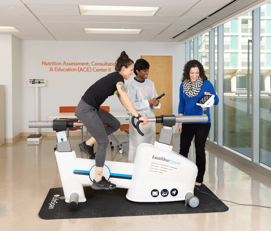 student being observed by two people as they ride an exercise bike