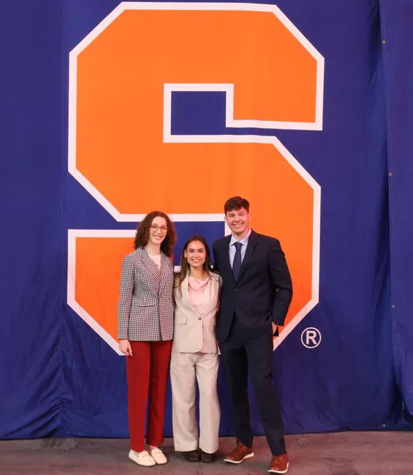 co-chairs of 2024 charity auction stand in front of big orange Syracuse "S" logo