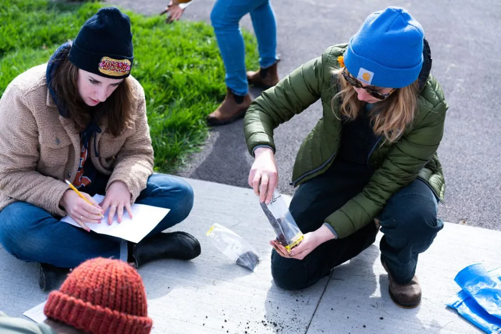 two female students dressed for colder weather sitting on sidewalk