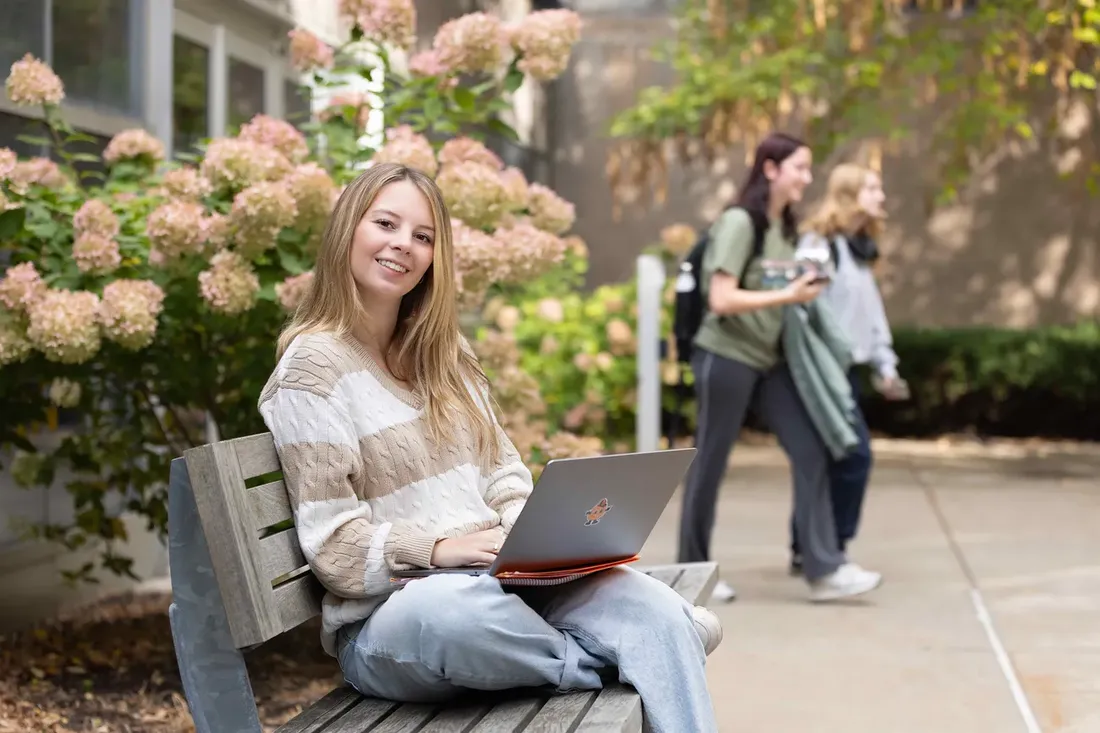 ambassador student sits on a bench with her laptop.