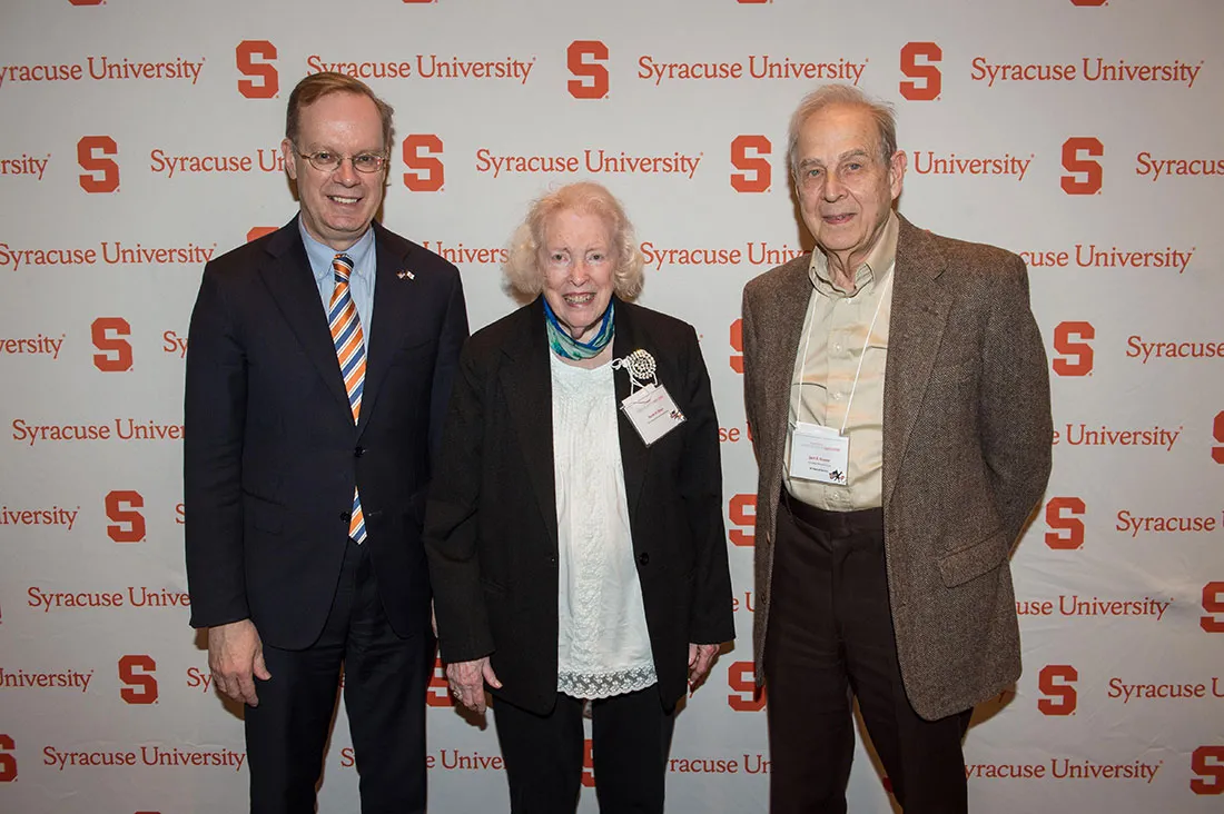 three people standing together against a wall with SU , from left to right male, female and male