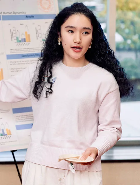 student long dark hair and light sweater presenting a poster she created