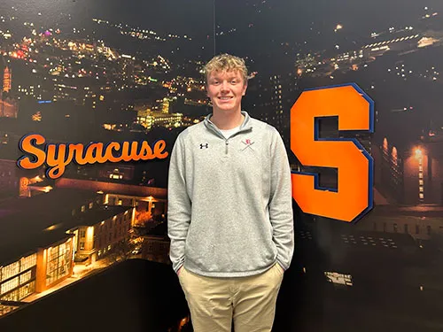 Tall blonde standing in front of a Syracuse University logo