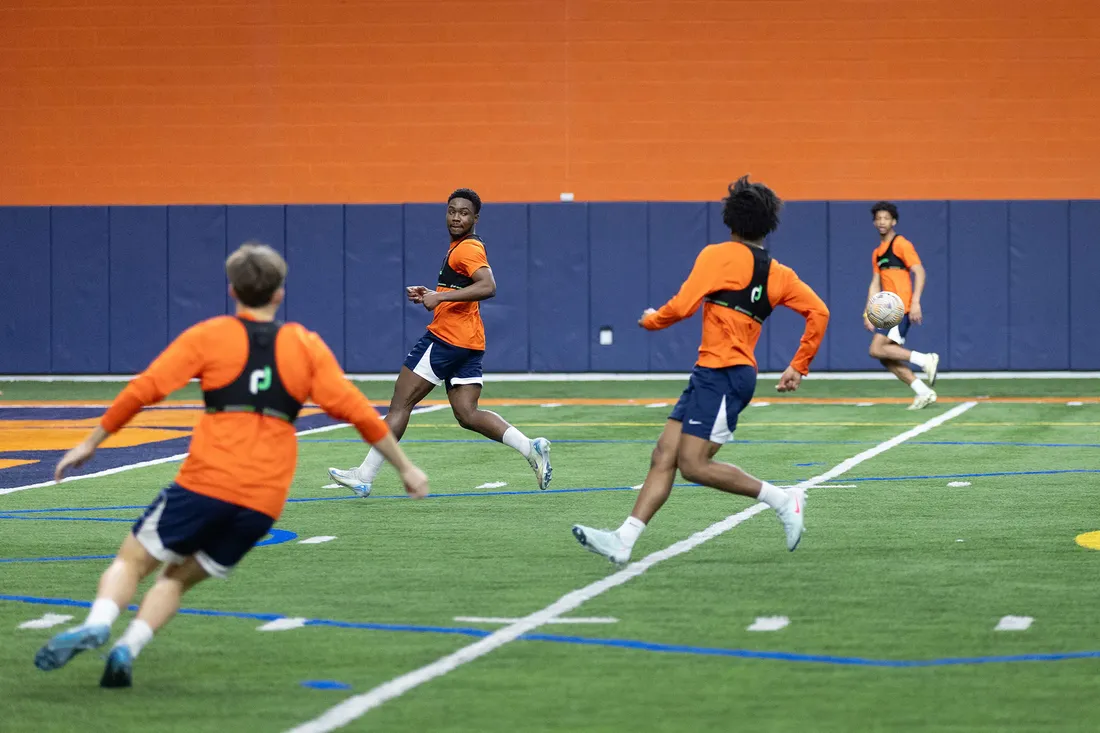 four male students playing soccer on athletic field