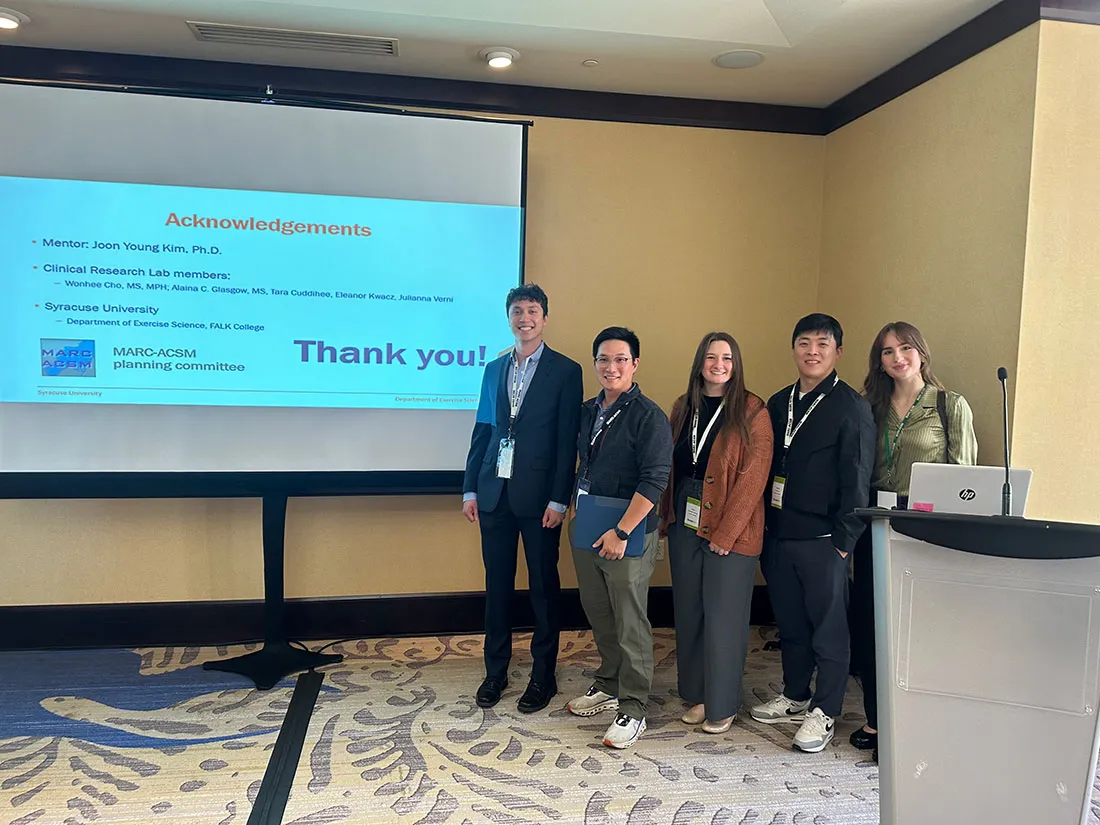 five people standing next to a projection screen