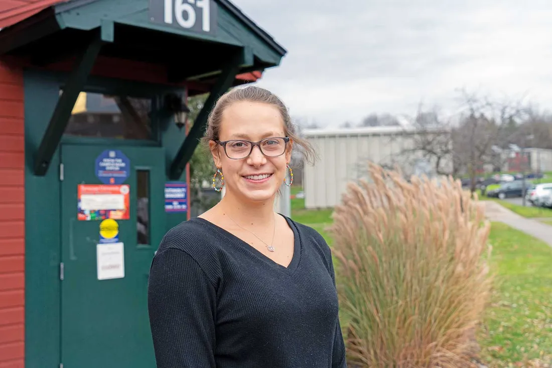 female student in dark shirt with hair pulled back and glasses standing outside building on south campus