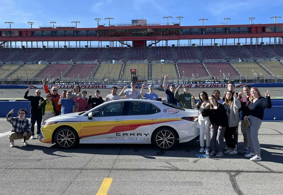 students standing on speedway next to NASCAR pace car