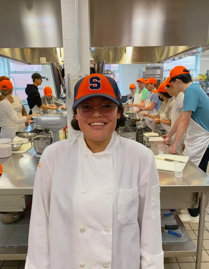 student wearing chef whites standing in Falk kitchen with other students in the background