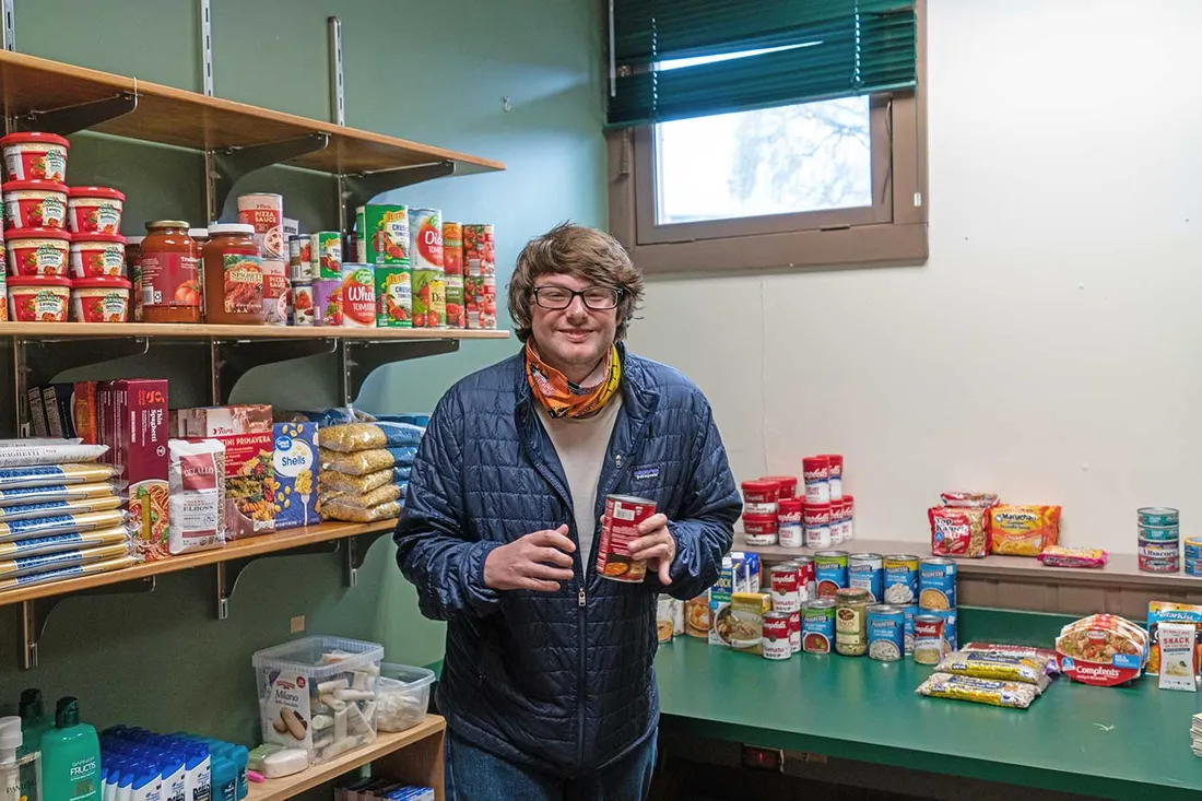 young man standing in food pantry surrounded by nonperishable items