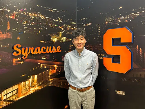 student NIcholas standing in front of Syracuse University logo
