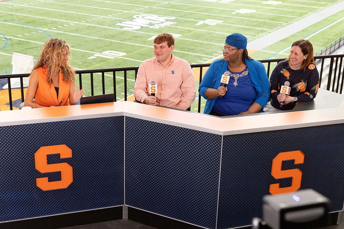 announcer and 3 students sit at sidelines booth at the dome