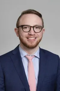 portrait of young man with short brown hair, wearing suit and pink tie, wearing glasses