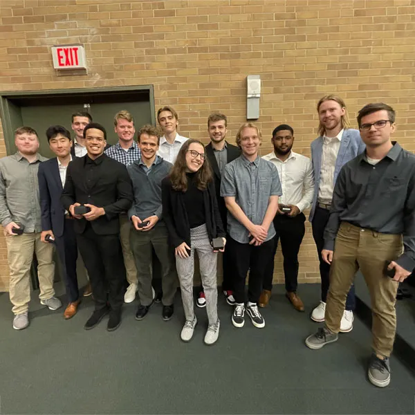 thirteen male and female students standing in a group outside a brick building
