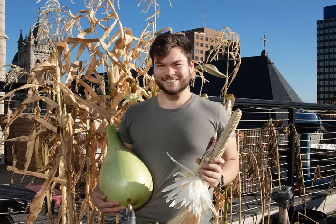 male student holding gourds infront of dried corn stalks