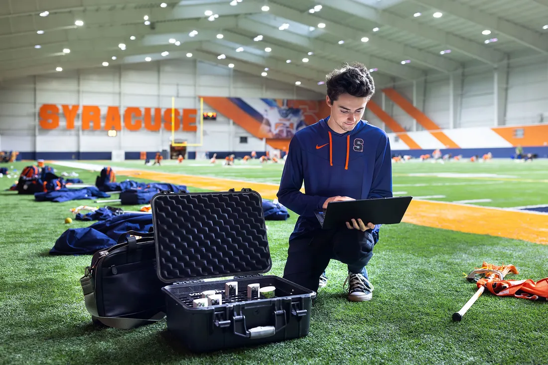 student checking out gps device while squatting on the sidelines during women's lacrosse practice