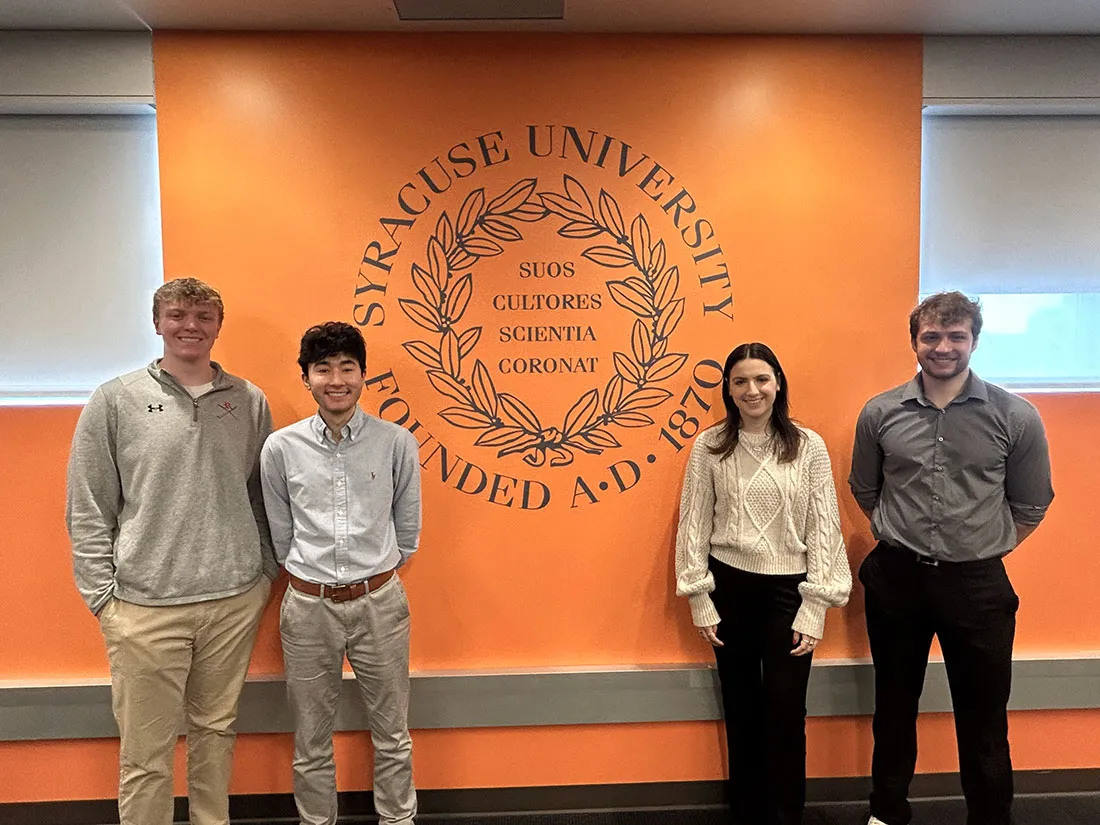 four student national collegiate sports analytics champions standing in front of SU logo