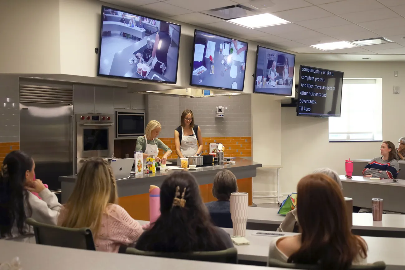 People are seated watching a live cooking presentation.