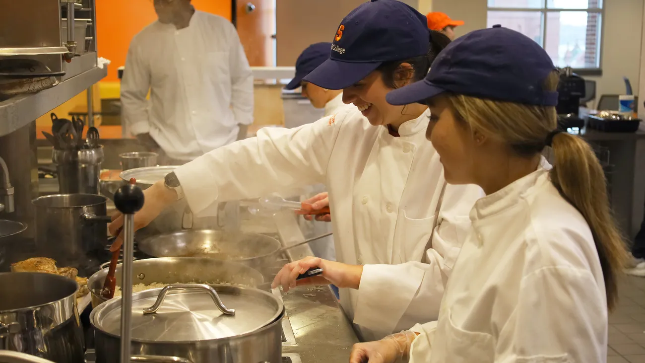 students wearing baseball hats and white chef jackets cooking in class