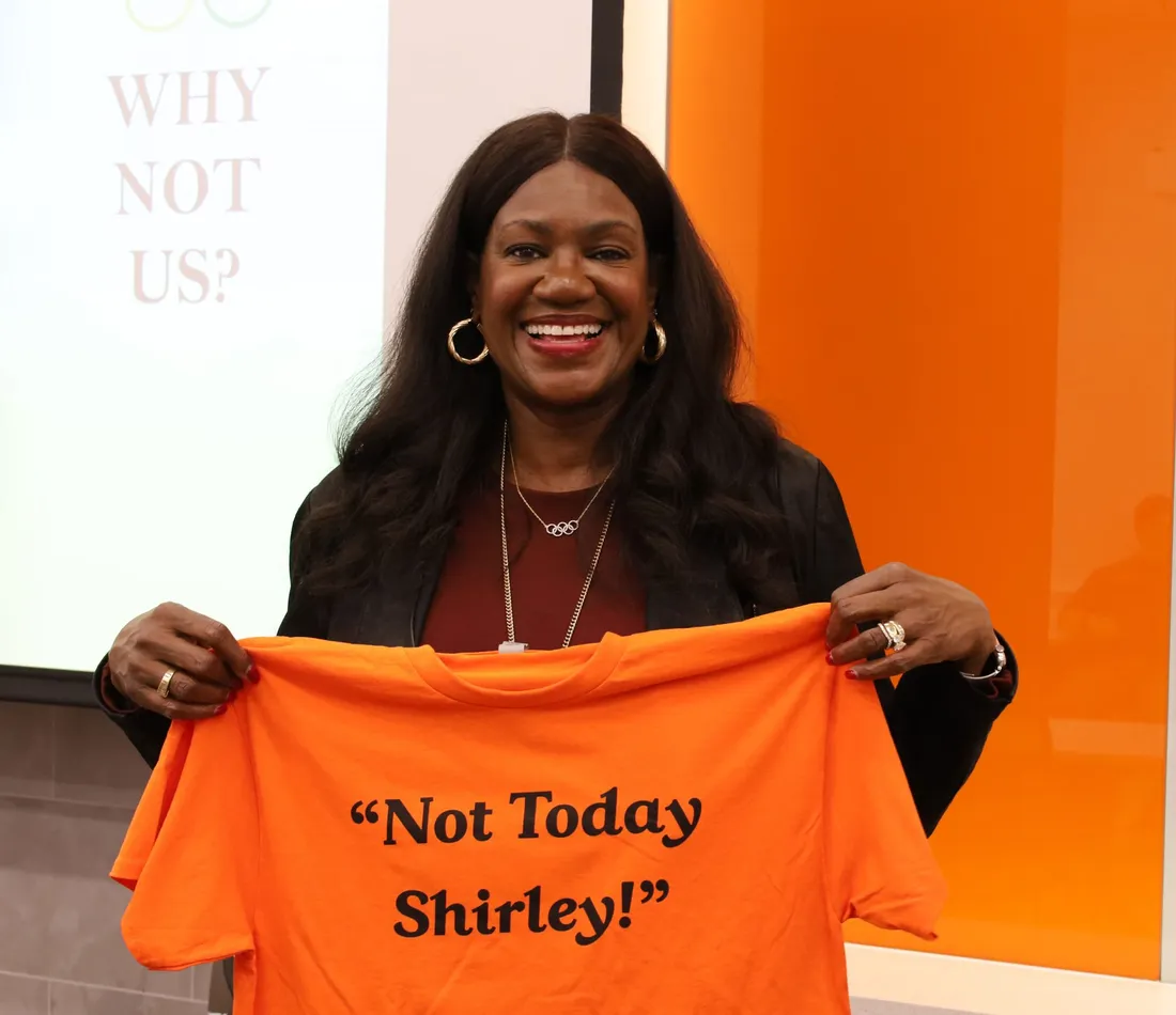 woman holding up orange t shirt in front of her that says Not today Shirley