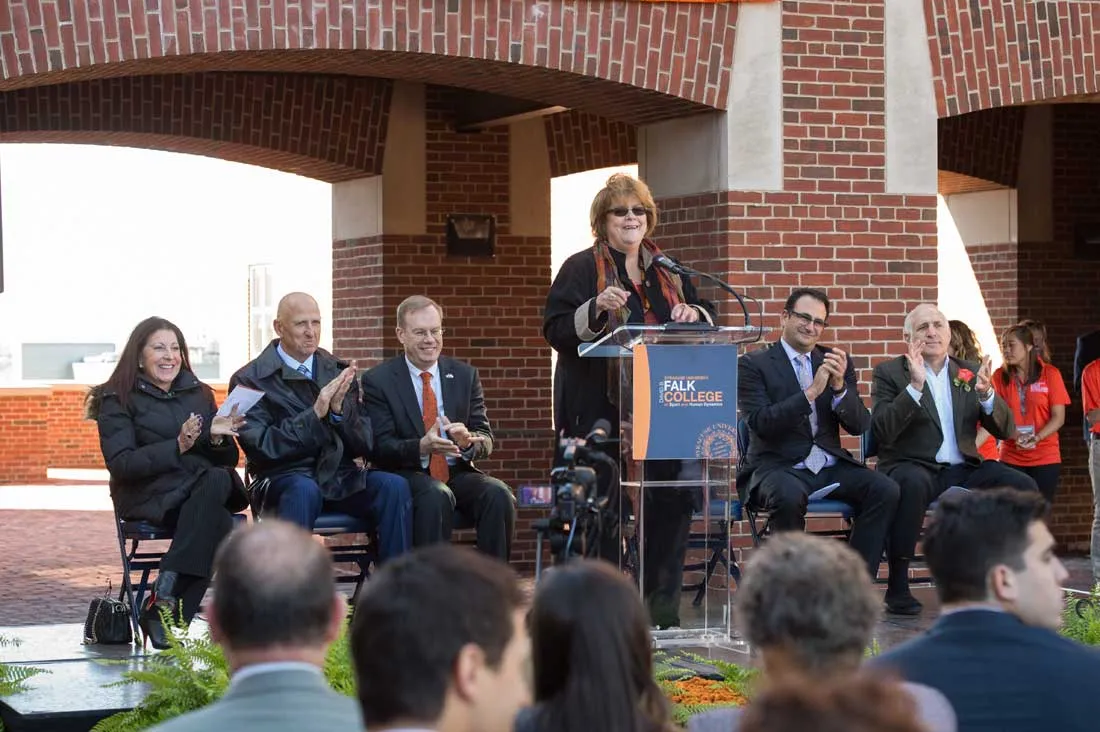 Diane Murphy on the patio in front of a podium surrounded by people in chairs and attendees in front of her seated in chairs