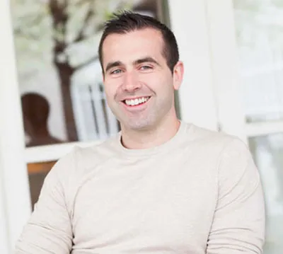 man with dark hair wearing a sweater smiling