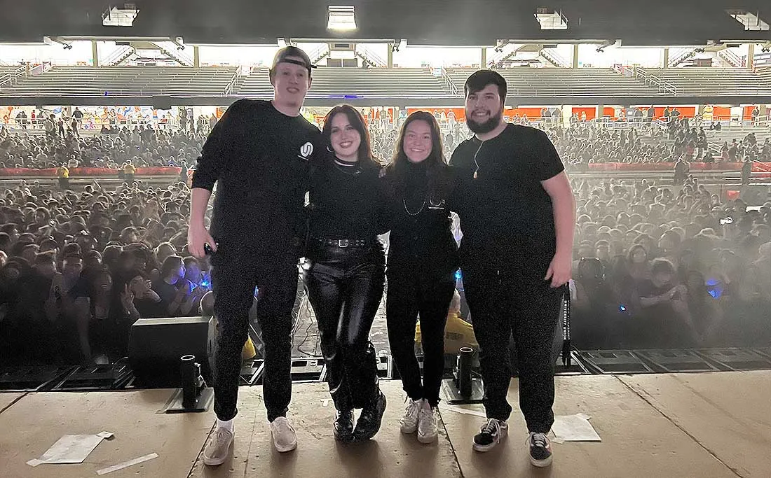 four university union members standing on stage at JMA wireless dome with a crowd behind them