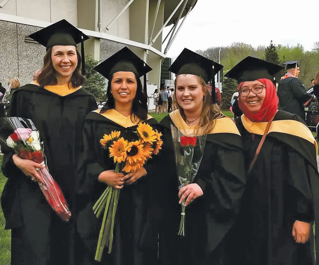 four female food studies graduates standing together in cap and gown