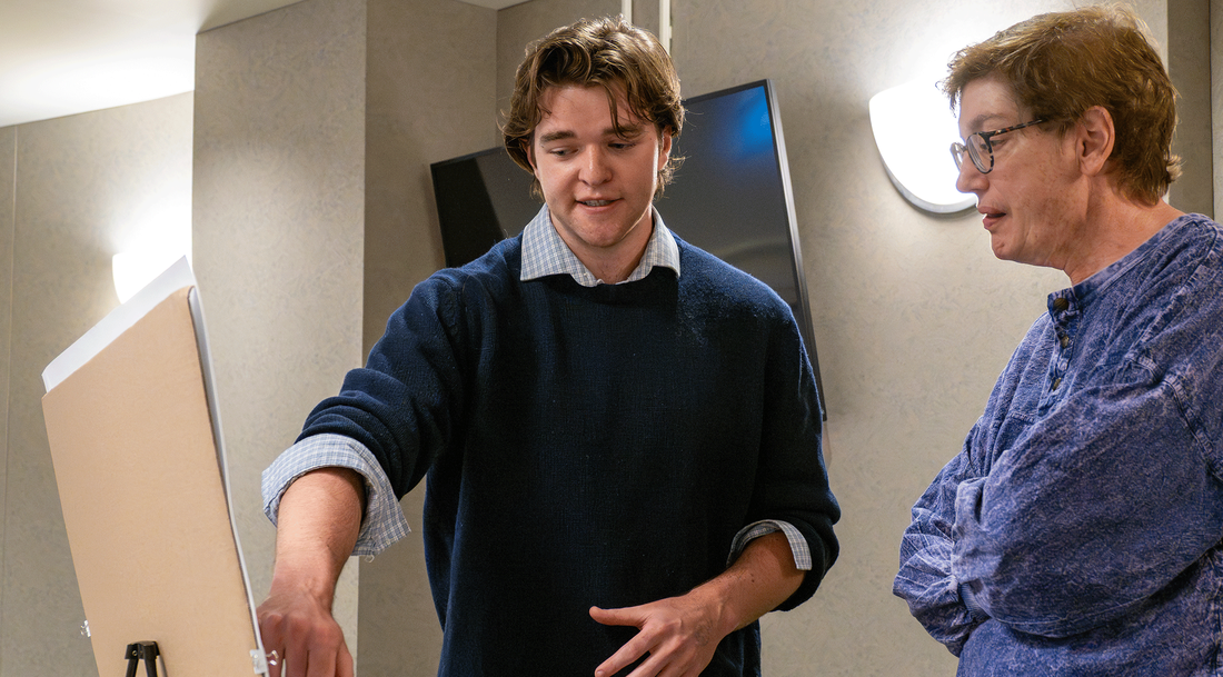 male student presenting his poster to a woman