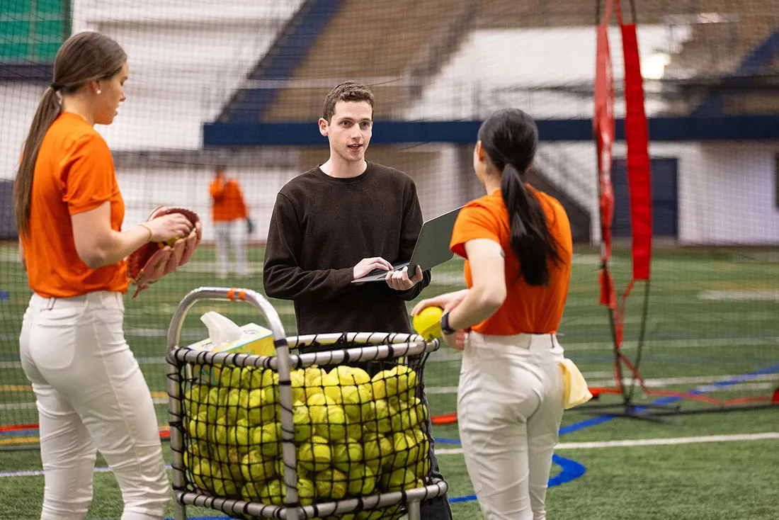 students talking standing in front of cart full of softballs