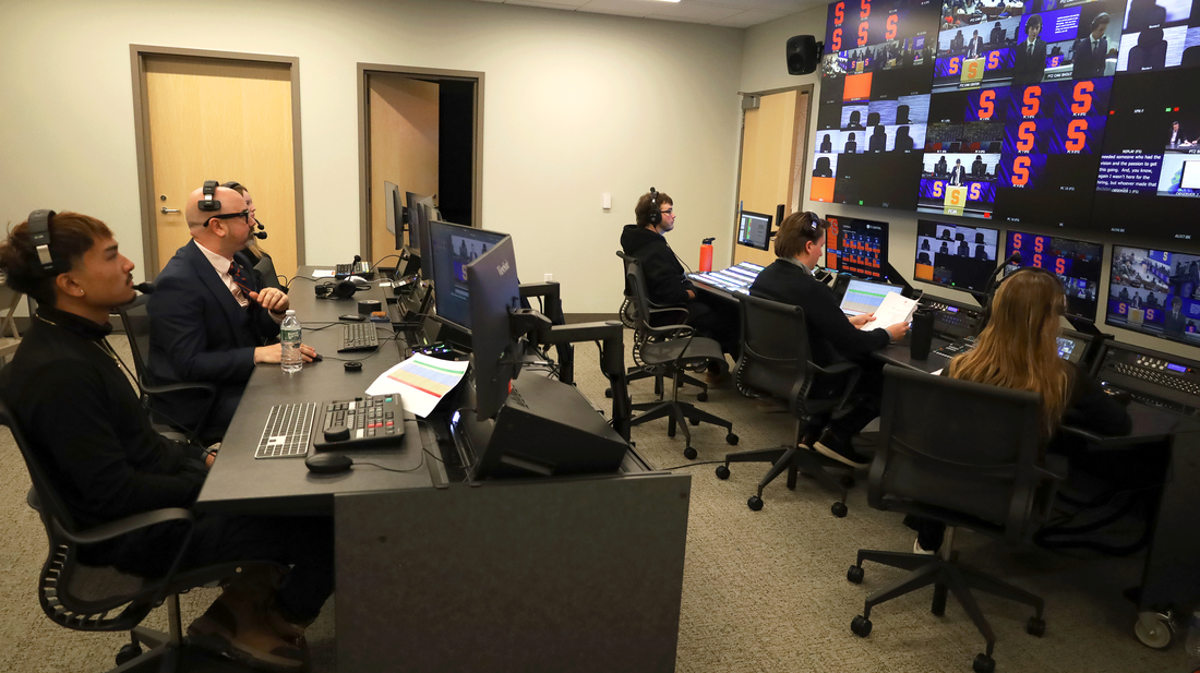 A group of people working at desks in a control room, focused on monitors and communication equipment.