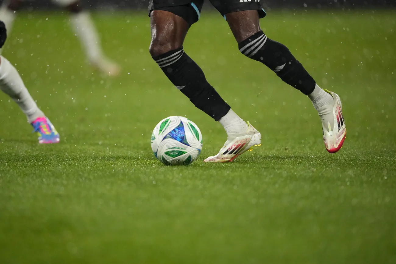 Legs of a soccer player getting ready to kick the ball across the field with other players close by