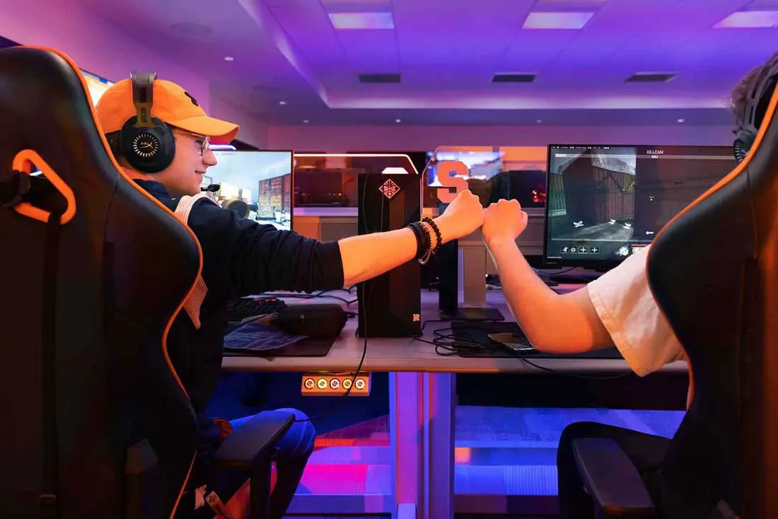two students bumping fists as they sit side by side at the new esports gaming statioins