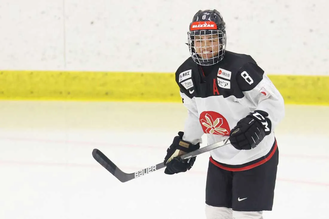young woman in hockey gear with stick in hand standing on the ice