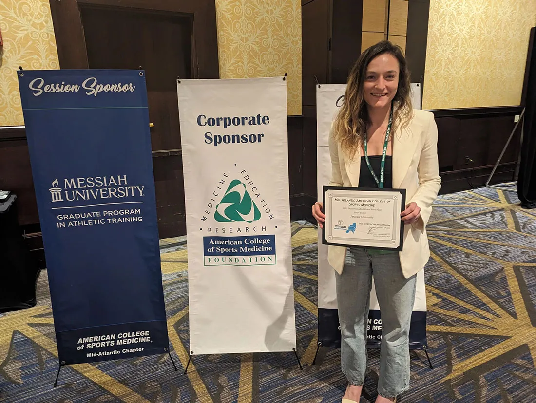 female student standing by poster and holding award certificate