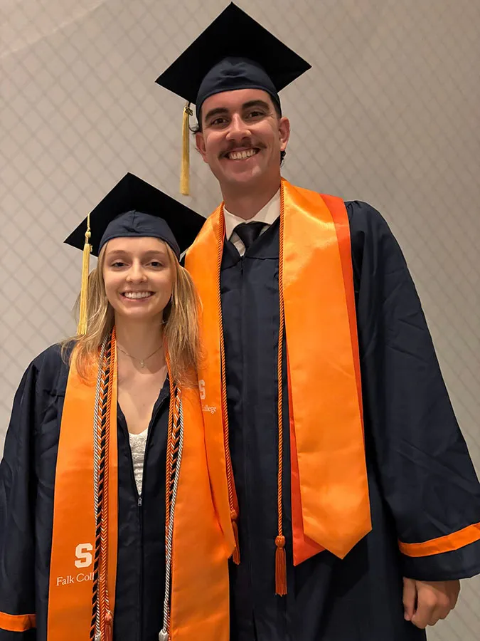 Marshals Piper Evans and Steven Chuck dressed in graduation cap and gown, pose standing next to each other.