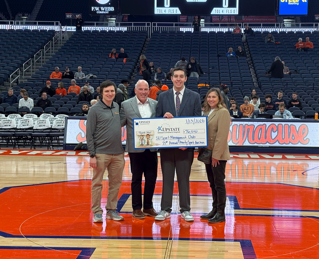 Four people standing side by side displaying check presented at Sport Management Charity Auction