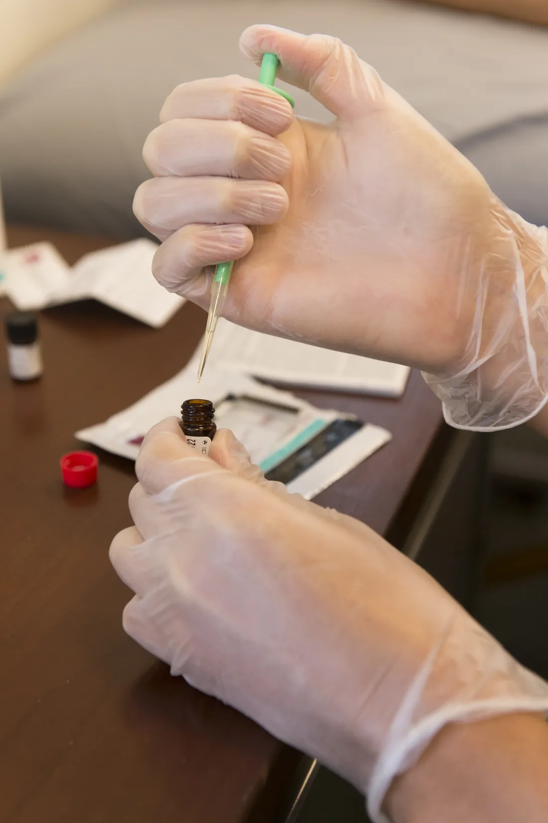 gloved hands are injecting a liquid into a vile