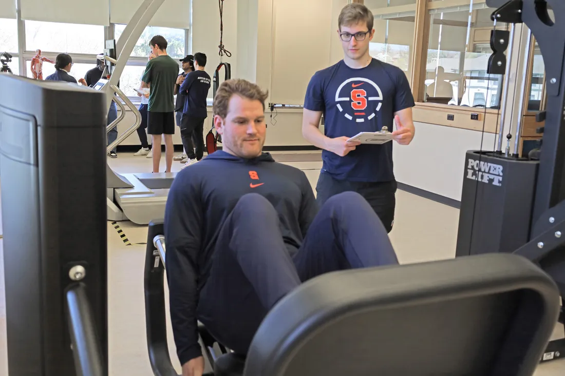 A student researcher is examining a student athlete at a weight machine