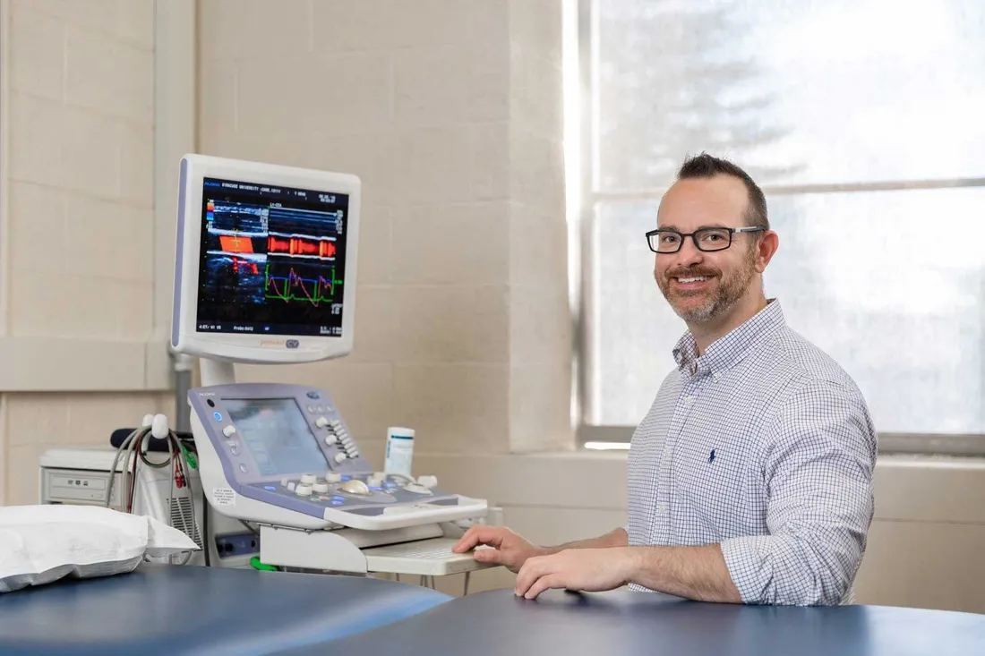 male professor in lab sitting behind examination bed and diagnostic equipment with computer screen