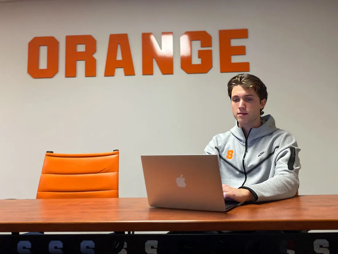 male student in SU hoodie sitting at desk looking at computer