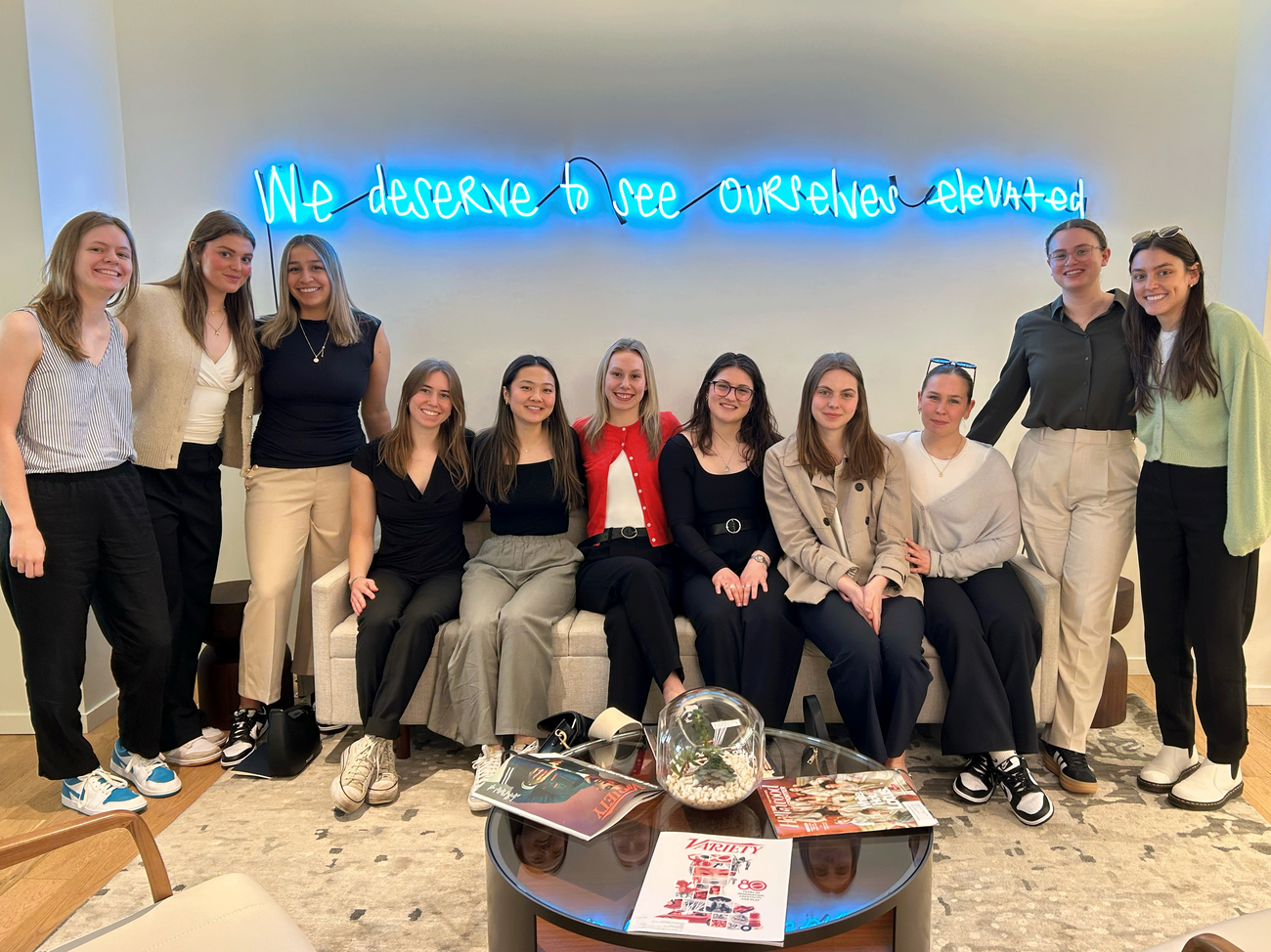 Falk College students, some seated some standing, in front of a light-up sign that says "We Deserve to See Ourselves Elevated."