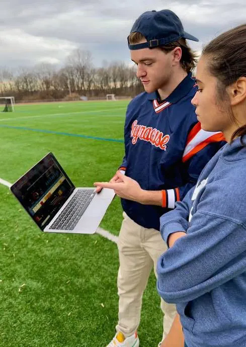 male and female student on athletic field looking at a computer