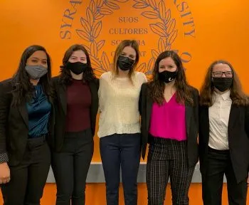 five women wearing masks because of COVID standing in front of orange wall with SU logo