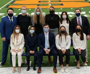 eleven sports management students posing together. back row six students and five in front all wearing masks