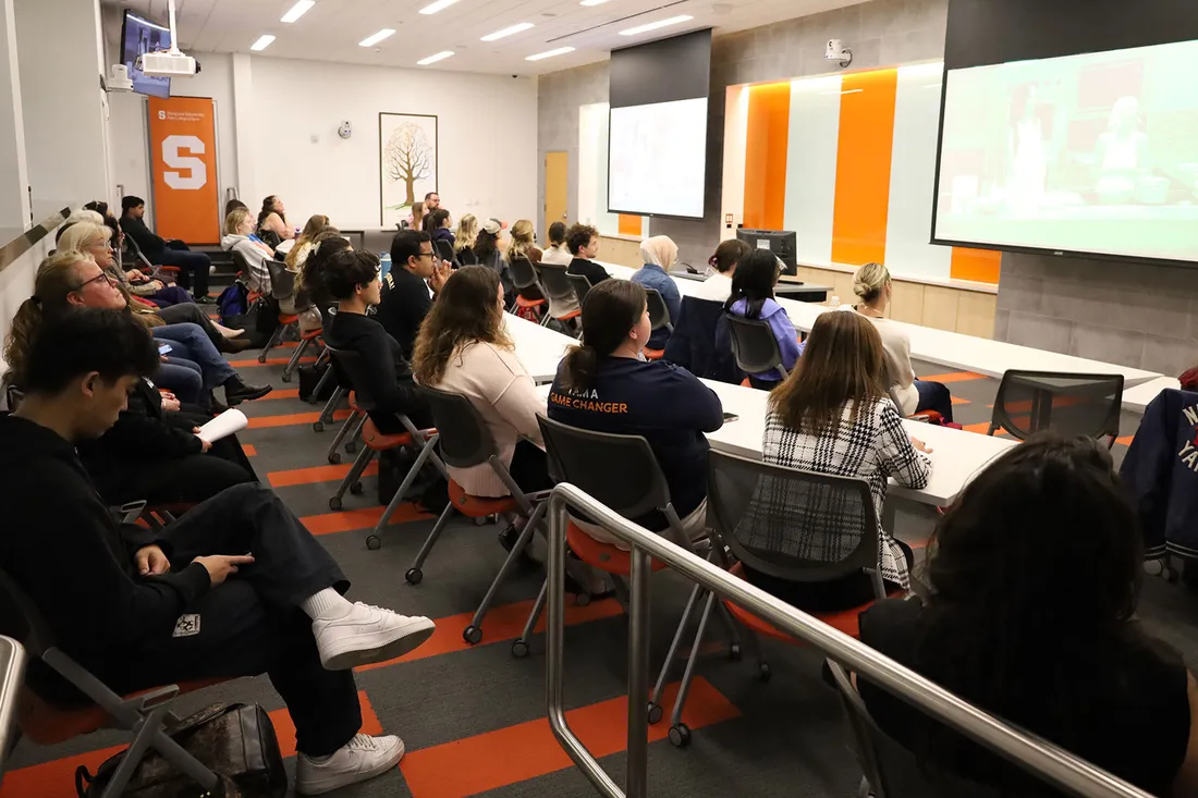 A crowd of people are seated watching a presentation on two screens.