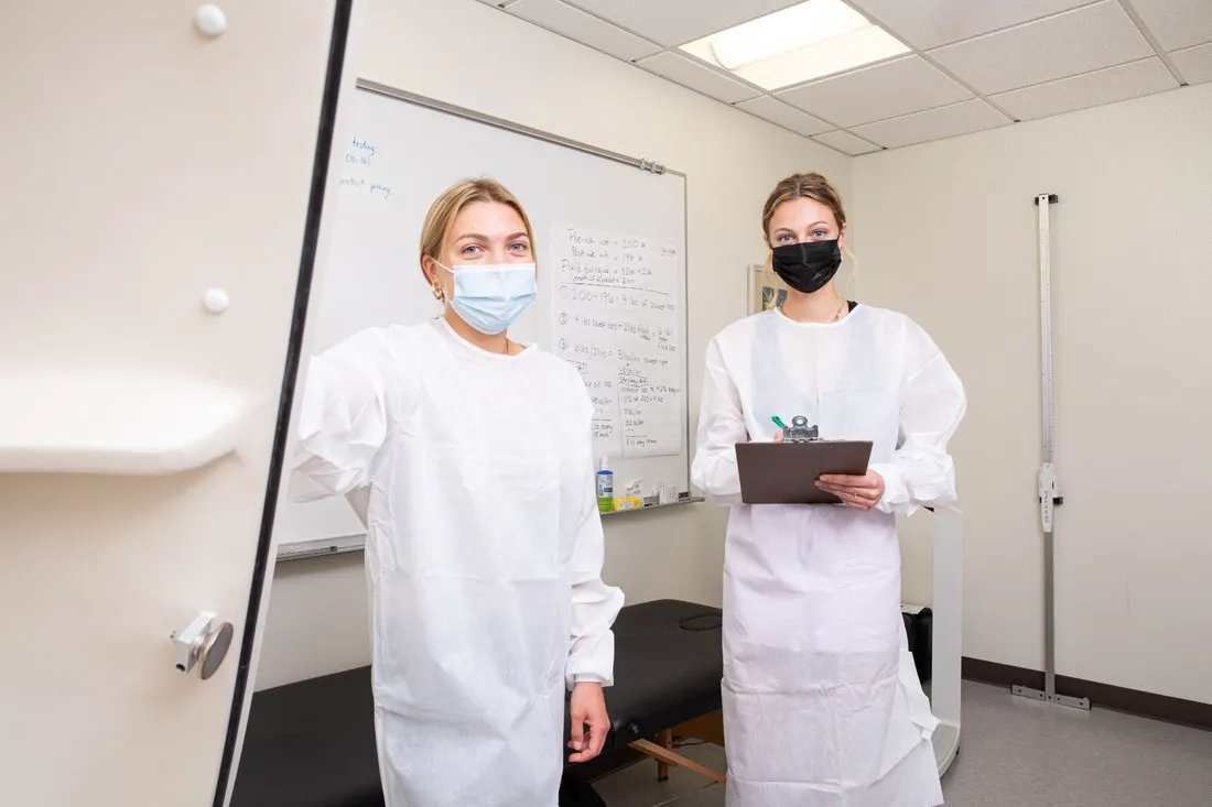 two female student scholars dressed in white medical gowns with masks