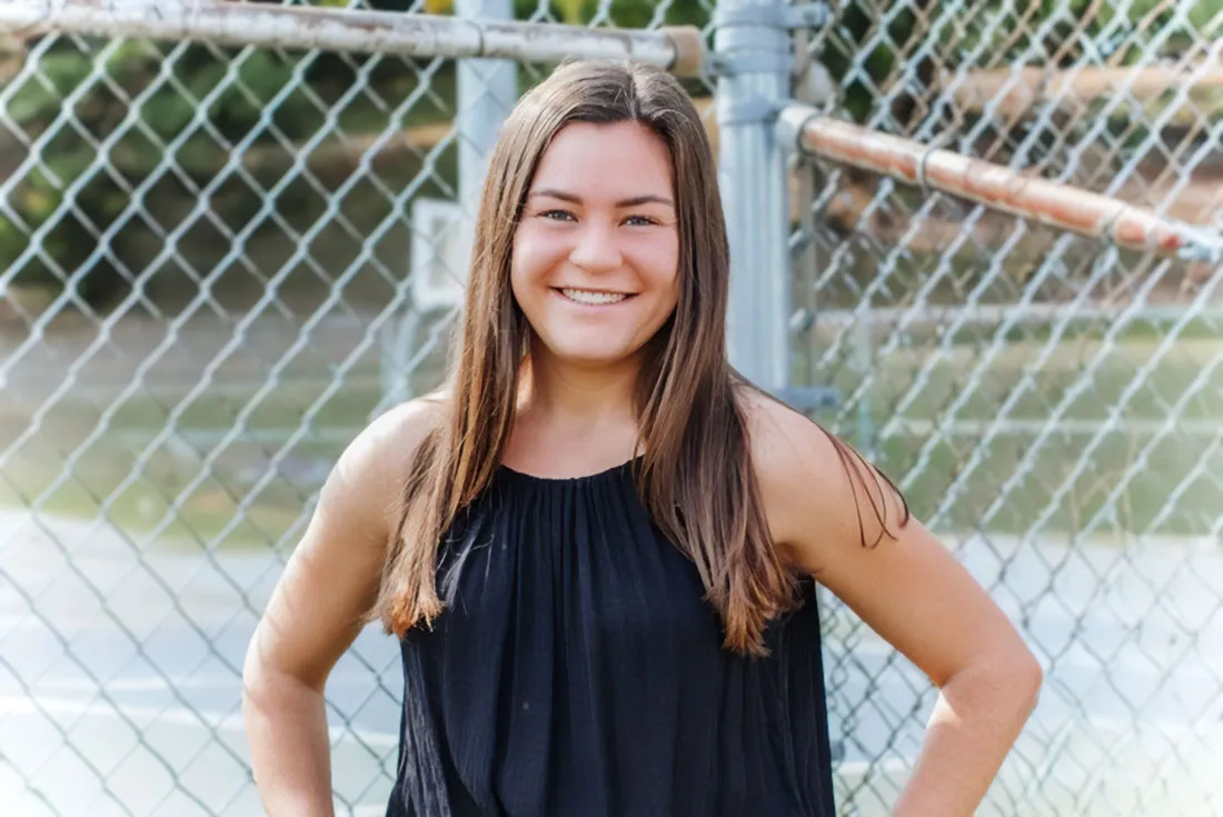 young women in black shirt standing in front of a chain link fence