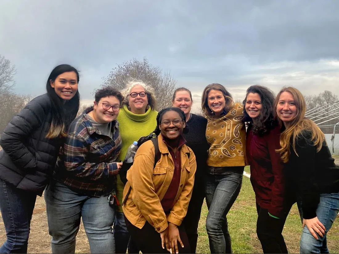 eight women standing together outside in an open field