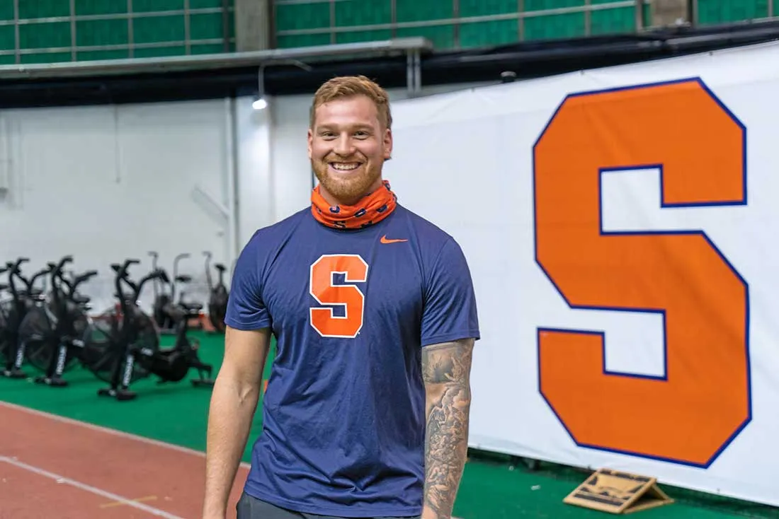 male student wearing blue tshirt with orange S on front with bandana around next standing on SU track