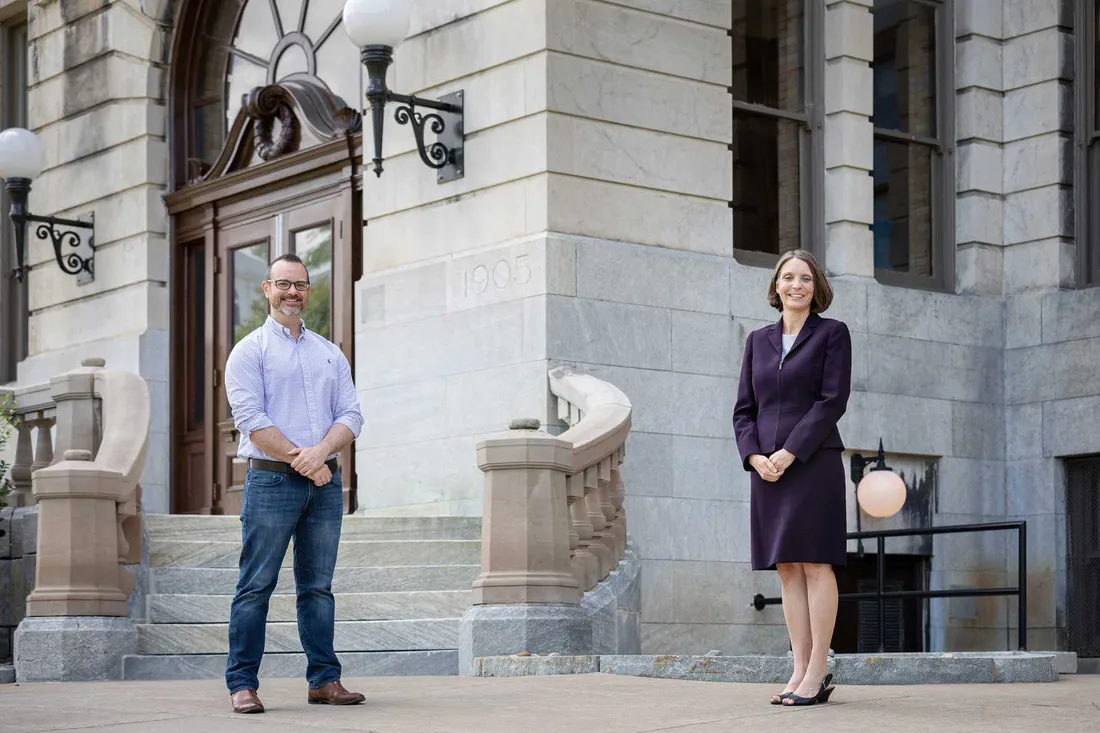 a male and female professor standing in front of gray brick building on SU campus
